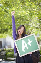 Excited mixed race female student holding a chalkboard with A+ written on it