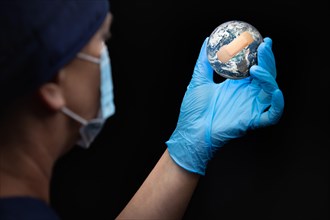 Nurse or doctor wearing face mask and surgical gloves holding bandaged planet earth