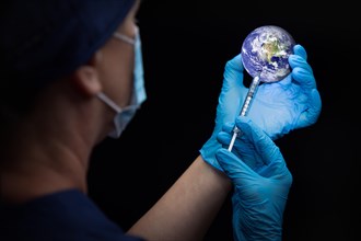 Doctor or nurse administiring vaccine through syringe into the planet earth