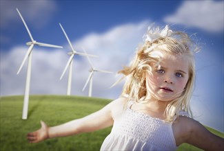 Beautiful young girl playing near wind turbines and grass field