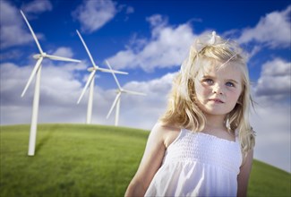 Beautiful young blue eyed girl playing near wind turbines and grass field