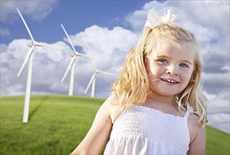 Beautiful young girl playing near wind turbines and grass field