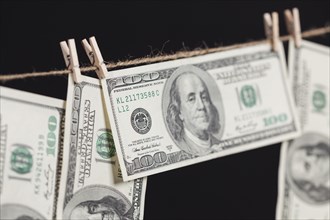 Hundred dollar bills hanging from a clothesline on a dark background