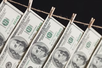 Hundred dollar bills hanging from a clothesline on a dark background