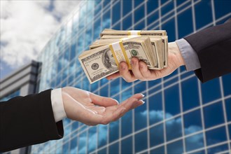 Male hand handing stack of cash to woman with corporate building
