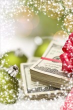 Stack of one hundred dollar bills with red bow near green christmas ornaments on snow flakes with snow flake border