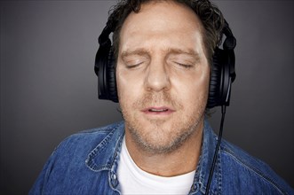 Man with eyes shut wearing headphones enjoying his music on a grey background