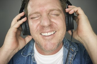 Man with eyes shut wearing headphones enjoying his music on a grey background