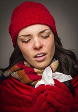 Sick mixed-race woman wearing winter hat and gloves blowing her sore nose with a tissue
