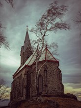 Church on a hill surrounded by trees with cloudy sky