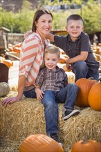 Attractive mother and her two sons pose for a portrait in a rustic ranch setting at the pumpkin patch