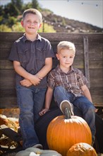 Two young boys at the pumpkin patch leaning against antique wood wagon