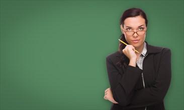 Serious young woman with pencil and glasses in front of blank chalk board