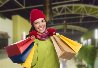 Pretty warmly dressed mixed-race woman in outdoor mall with shopping bags