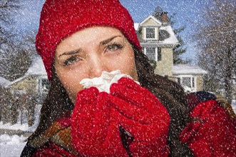 Miserable sick woman in falling snow blowing her sore nose with tissue outside
