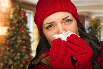 Sick mixed race woman blowing her sore nose with tissue in christmas setting