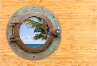 Antique porthole with tropical beach view on a bamboo wall background