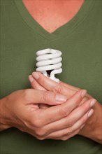 Female hands holding energy saving light bulb against green shirt
