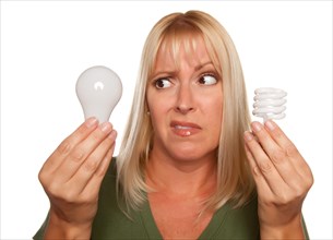 Funny faced woman holds energy saving and regular light bulbs isolated on a white background