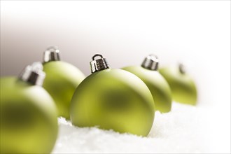 Green christmas ornaments on snow flakes over a grey background
