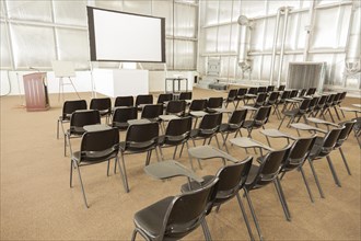 Empty presentation conference room with desk chairs and projector screen