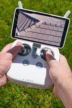 Hands holding drone quadcopter controller with residential roof image on screen