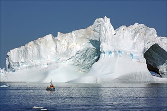 Small fishing boat in front of huge iceberg with two holes