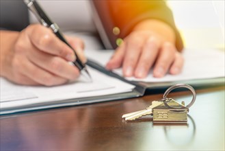 Woman signing real estate contract papers with house keys and home keychain in front