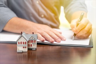 Man signing real estate contract papers with small model home in front