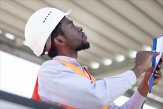 Young black man working outside as technician with helmet and safety vest