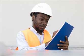 Young black man working outside as technician with helmet and safety vest
