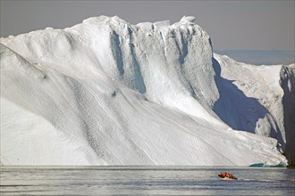 Small boat with passengers in front of huge iceberg