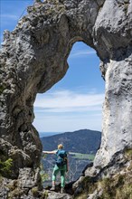 Hiker standing in the rock gate Breitensteinfensterl with view of high fog over the valley