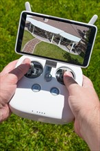 Hands holding drone quadcopter controller with overhead of house on screen
