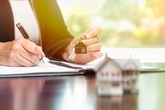 Woman signing real estate contract papers holding house keys and home keychain with small model home in front