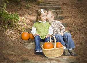Adorable brother and sister children sitting on wood steps with pumpkins whispering secrets or kissing cheek