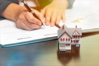 Man signing real estate contract papers with small model home in front