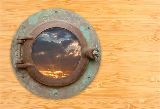 Antique porthole with view of sunset on a bamboo wall background