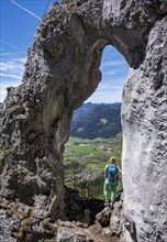 Hiker standing in the rock gate Breitensteinfensterl with view of high fog over the valley