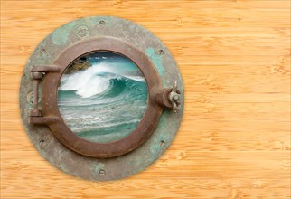 Antique porthole with view of crashing waves on a bamboo wall background