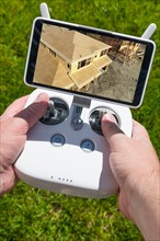 Hands holding drone quadcopter controller with construction house framing on screen
