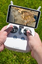 Hands holding drone quadcopter controller with construction house framing on screen
