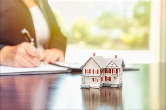 Woman signing real estate contract papers with small model home in front