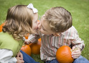 Cute young brother and sister children kissing among the pumpkins at the pumpkin patch