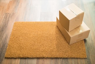 Blank welcome mat on wood floor with shipment of boxes