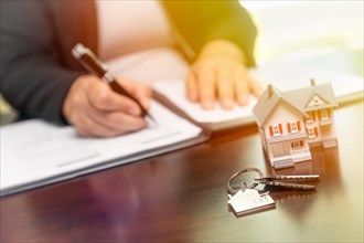 Woman signing real estate contract papers with house keys