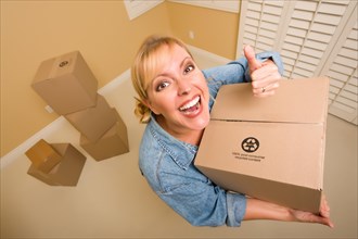 Excited woman with thumbs up and moving boxes in empty room taken with extreme wide angle lens