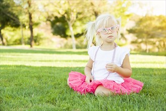 Cute little girl playing dress in the grass up with pink glasses and beaded necklace