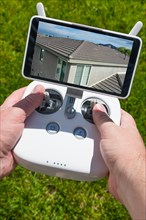 Hands holding drone quadcopter controller with residential roof image on screen