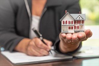 Woman signing real estate contract papers holding small model home in front